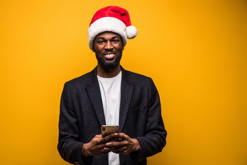 Young african man in santa hat use on the phone isolated on yellow background