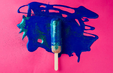 Sausage on sticks in blue sparkle paint. On a pink and orange textured background, top view photo.