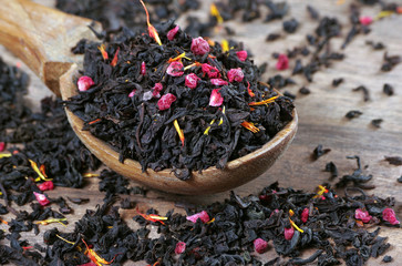 black blended tea with flower petals and dried fruit on a wooden spoon.