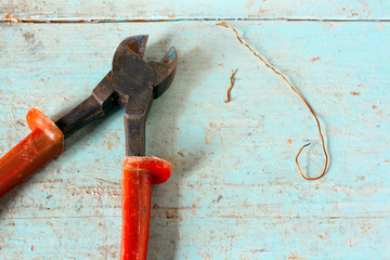 Used nippers with copper wire on rustic light blue wooden surface