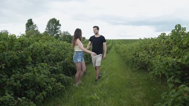 Lovely couple walks among currant plantation, twists on hands