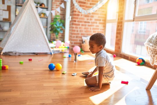 Beautiful african american toddler playing with cars around lots of toys at kindergarten