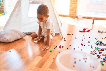 Beautiful african american toddler playing with cars around lots of toys at kindergarten