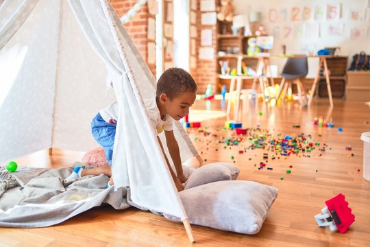 Beautiful african american toddler playing inside tipi smiling at kindergarten