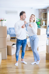 Young beautiful couple standing drinking cup of coffee at new home around cardboard boxes