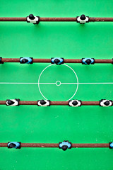 Toy football players on a green soccer field, table football game flat aerial view.