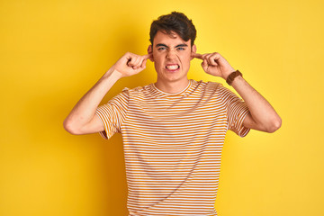 Teenager boy wearing yellow t-shirt over isolated background covering ears with fingers with...