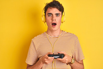 Teenager boy playing video games using gamepad over isolated yellow background scared in shock with...