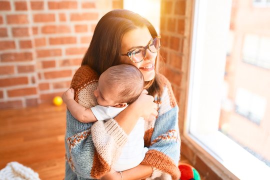 Young beautifull woman and her baby standing at home. Mother holding and hugging newborn