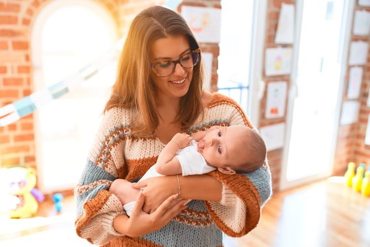 Young beautiful woman and her baby standing at home. Mother holding and hugging newborn