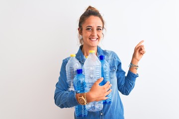 Young redhead woman holding plastic bottle to recycle over isolated background very happy pointing with hand and finger to the side