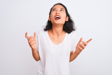 Young chinese woman wearing casual t-shirt standing over isolated white background crazy and mad shouting and yelling with aggressive expression and arms raised. Frustration concept.