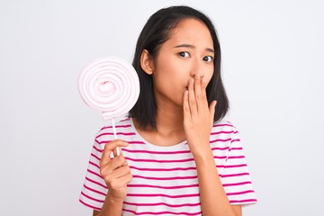 Young beautiful chinese woman eating lollipop standing over isolated white background cover mouth with hand shocked with shame for mistake, expression of fear, scared in silence, secret concept