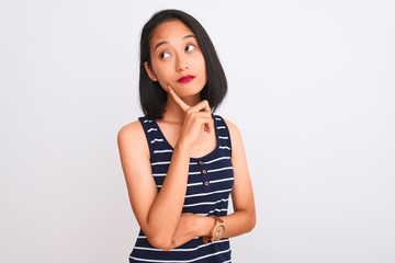 Young chinese woman wearing striped t-shirt standing over isolated white background with hand on chin thinking about question, pensive expression. Smiling with thoughtful face. Doubt concept.