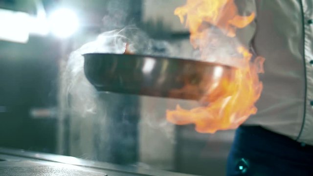 Chef cooks meat on an open fire in a burning pan