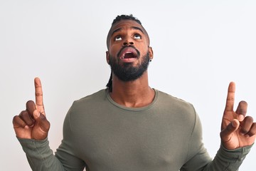 African american man with braids wearing green sweater over isolated white background amazed and surprised looking up and pointing with fingers and raised arms.