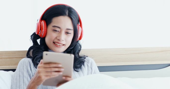 Smiling beautiful Asian woman lying on the bed and using tablet computer in the bedroom in the morning.