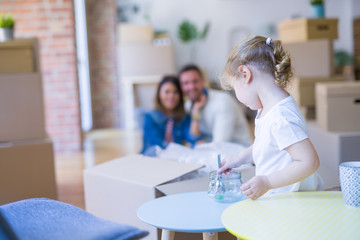 Obraz premium Beautiful family sitting on the floor playing with his kid at new home around cardboard boxes