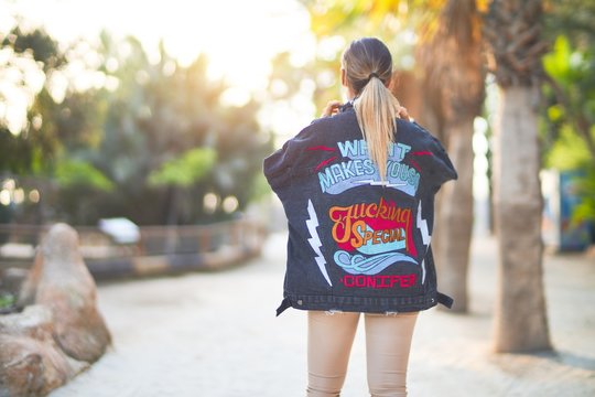 Young beautiful woman wearing denim jacket standing backwards at the town park