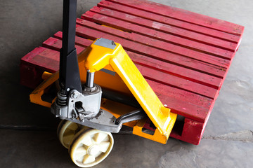 Yellow hand pallet truck with red wooden pallet