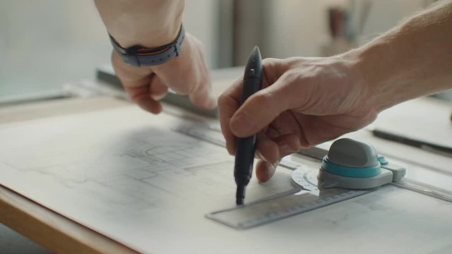 Engineer draws buildings on the table using a pencil and ruler. An architect creates a building design on paper using a marker and ruler