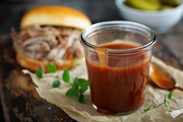 Homemade sweet and spicy barbeque sauce with a basting brush in a jar, pulled pork sanswich in the...
