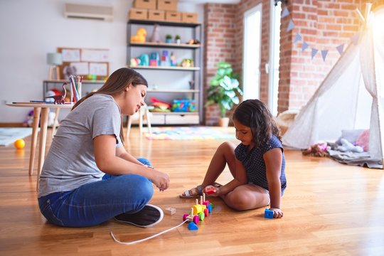 Beautiful teacher and toddler girl playing with train at kindergarten
