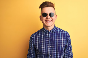 Obraz premium Young handsome man wearing casual shirt and sunglasses over isolated yellow background with a happy and cool smile on face. Lucky person.