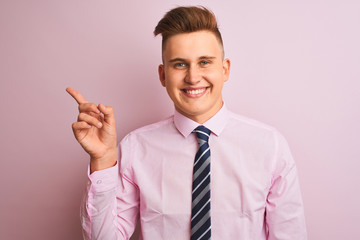 Young handsome businessman wearing shirt and tie standing over isolated pink background with a big smile on face, pointing with hand finger to the side looking at the camera.