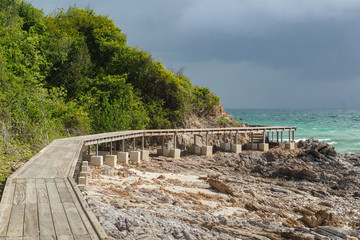 Fototapeta na wymiar Wooden footbridge on a rocky seashore against the backdrop of a thunderstorm.