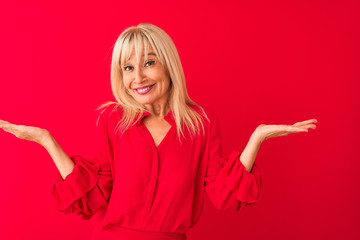 Middle age woman wearing elegant shirt standing over isolated red background clueless and confused...