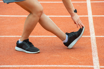 Cropped shot view of runner woman doing stretching and warming up her legs before running in the running track in stadium. The benifit of stretching can increasing flexibility and reduce injury.