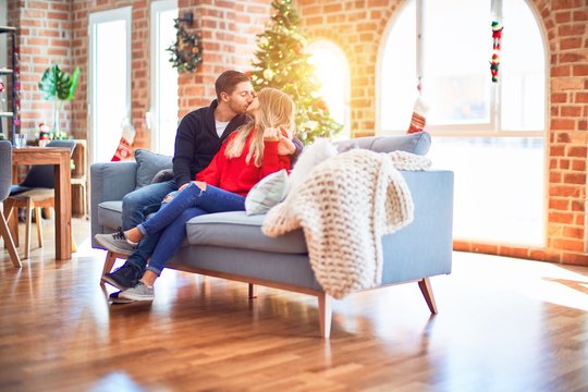 Young beautiful couple smiling happy and confident. Sitting on the sofa hugging and kissing around christmas tree at home