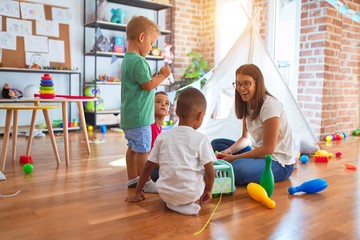Young beautiful teacher and toddlers playing around lots of toys at kindergarten
