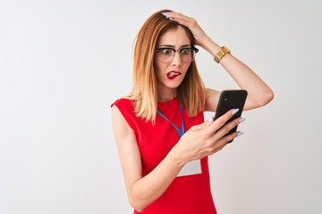 Naklejka premium Redhead businesswoman wearing id card using smartphone over isolated white background stressed with hand on head, shocked with shame and surprise face, angry and frustrated. Fear and upset 