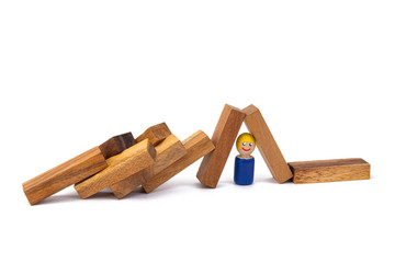 A wooden toy of a boy lies under a large number of obstacles in the form of wooden blocks on a white isolated background. The concept of overcoming difficulties and life hardships