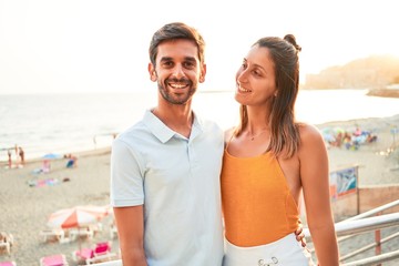 Young beautiful couple on vacation smiling happy and confident. Standing with smile on face hugging at the beach