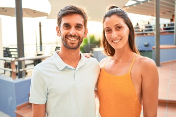 Young beautiful couple on vacation smiling happy and confident. Standing with smile on face hugging at the beach