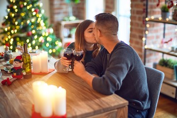Young beautiful couple smiling happy and confident. Toasting with cup of wine and kissing celebrating christmas at home