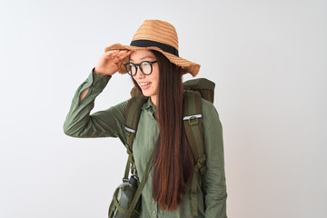 Chinese hiker woman wearing canteen hat glasses backpack over isolated white background very happy and smiling looking far away with hand over head. Searching concept.