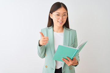 Obraz premium Young chinese student woman wearing glasses reading book over isolated white background happy with big smile doing ok sign, thumb up with fingers, excellent sign