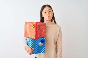 Young chinese woman holding birthday gifts over isolated white background making fish face with lips, crazy and comical gesture. Funny expression.