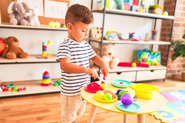 Beautiful toddler boy playing meals with plastic plates, fruits and vegetables at kindergarten