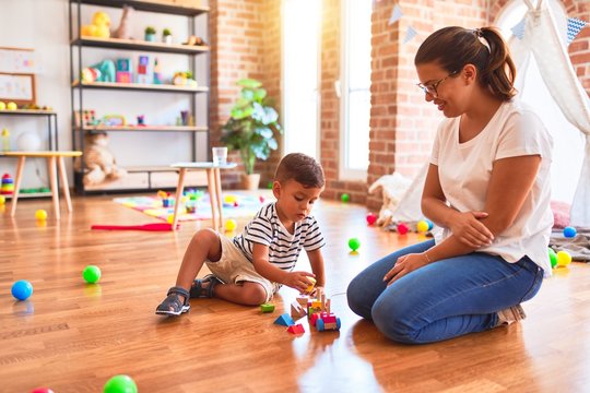 Beautiful teacher and toddler boy playing with train at kindergarten