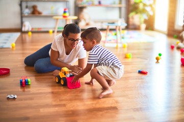 Beautiful teacher and toddler boy playing with tractor and cars at kindergarten