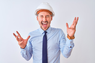 Young business man wearing contractor safety helmet over isolated background celebrating mad and crazy for success with arms raised and closed eyes screaming excited. Winner concept