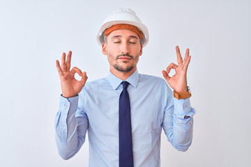 Young business man wearing contractor safety helmet over isolated background relax and smiling with eyes closed doing meditation gesture with fingers. Yoga concept.