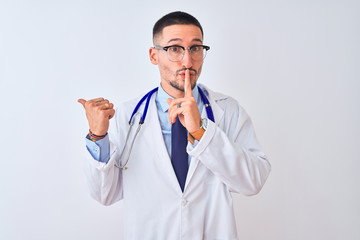 Young doctor man wearing stethoscope over isolated background asking to be quiet with finger on lips pointing with hand to the side. Silence and secret concept.