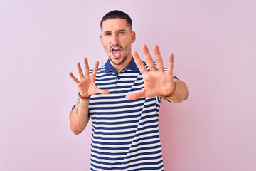 Young handsome man wearing nautical striped t-shirt over pink isolated background afraid and terrified with fear expression stop gesture with hands, shouting in shock. Panic concept.