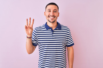 Naklejka premium Young handsome man wearing nautical striped t-shirt over pink isolated background showing and pointing up with fingers number three while smiling confident and happy.